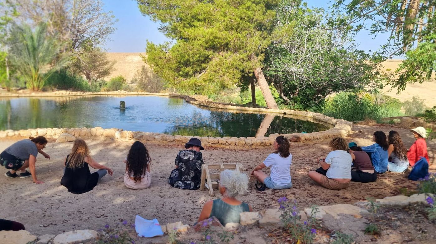 קבוצה יושבת במעגל סביב בריכה במדבר